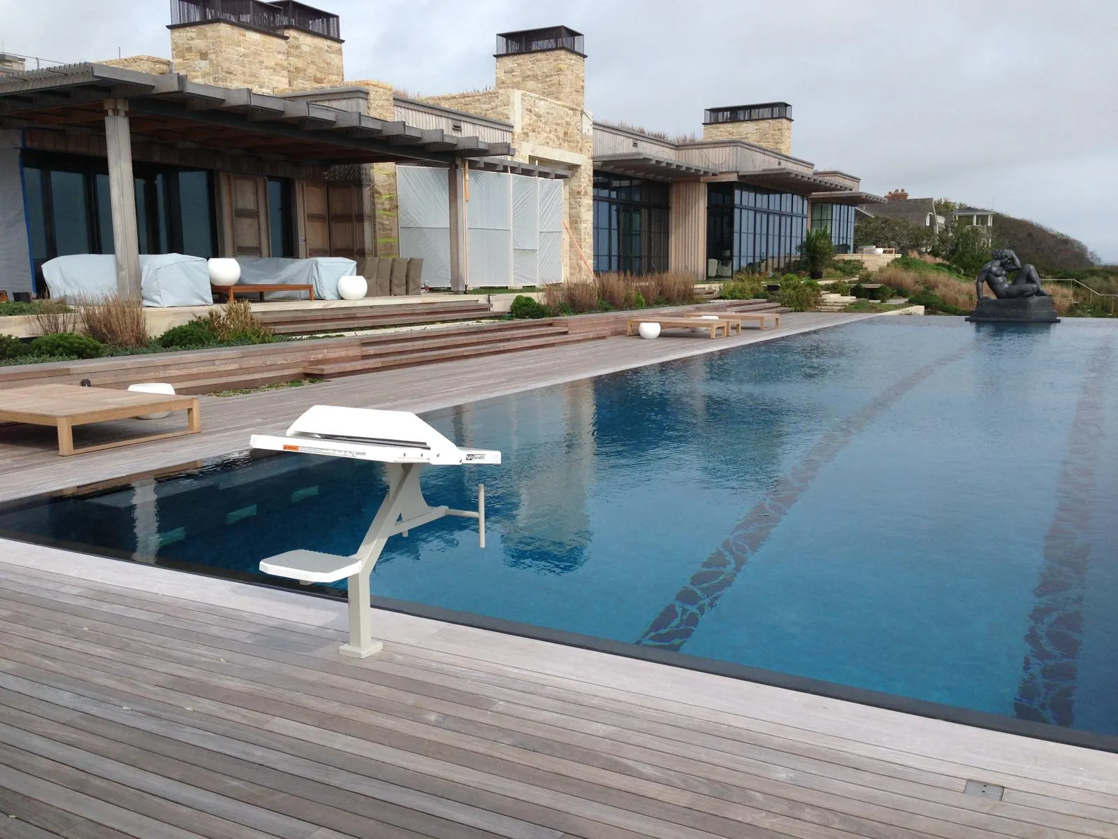 A lap pool with a starting block beside a weathered cedar deck, under an overcast sky.